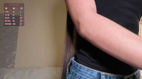 Video of a person's side, wearing blue jeans and a black top, with long, straight dark hair. Background shows a grey wall and a digital display with \"Lamborghini\" text.