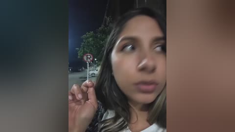 Video of a woman with long dark hair, wearing a white shirt, holding a fork, looking surprised at a man's erect penis on the right side of the image.