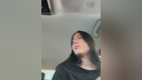 A blurred video shows a woman with long dark hair in a black shirt, standing in a modern, minimalistic room with white walls and recessed lighting.