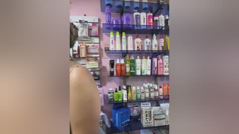 A video of a beauty salon with a tan arm and shoulder visible. Shelves stocked with various beauty products, including creams, lotions, and hair care products, in vibrant colors and containers.