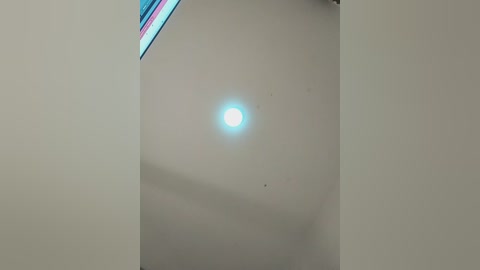Video of a bright, circular sun with a soft blue hue shining through a window with colorful, vertical panes. The room has a minimalist, modern aesthetic with a beige wall and clean lines.