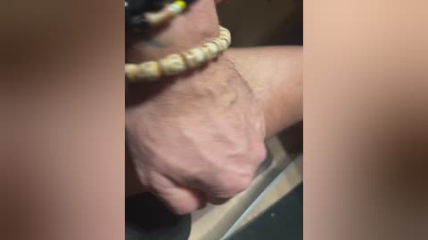 Media: A close-up video of a hand with a beige beaded bracelet, gripping a metal object, possibly a door handle, against a blurred background. The skin appears slightly wrinkled, and the hand is positioned at the center.