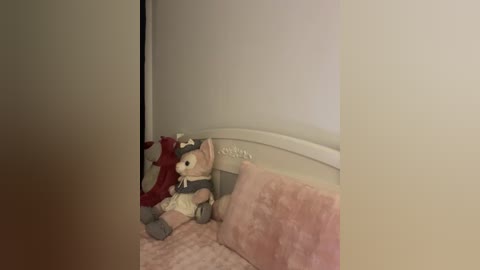 Video of a plush teddy bear and a red plush fox on a pink quilted bedspread, against a plain white wall, with a white headboard in a cozy, intimate bedroom setting.