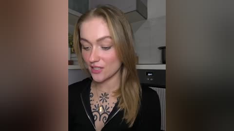 Video of a young Caucasian woman with blonde hair and light skin, wearing a black sweater with a floral design, standing in a modern kitchen with stainless steel appliances.