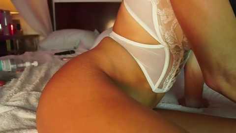 Video of a woman in white lace lingerie, kneeling on a bed with soft lighting, showcasing her curvy figure and detailed lingerie.