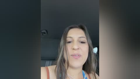 Video of a young woman with medium skin tone, straight brown hair, and a light blue top, captured indoors with a blurred background.