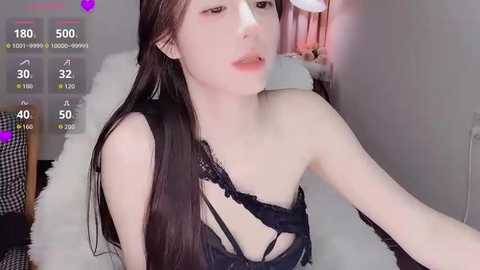 A young, slim, pale-skinned woman with long, dark hair, wearing a black lace bra, sits on a white fur rug in a bedroom. The image includes a virtual camera overlay showing stats and a purple heart.