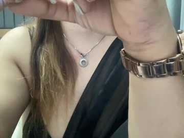 A video of a light-skinned woman with long brown hair, wearing a black strapless dress, a silver necklace, and a rose gold watch, captured from the neck up.