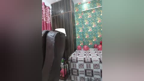 A video of a small, neatly arranged bedroom with floral wallpaper, red and black checkered bedspread, and a black leather chair.
