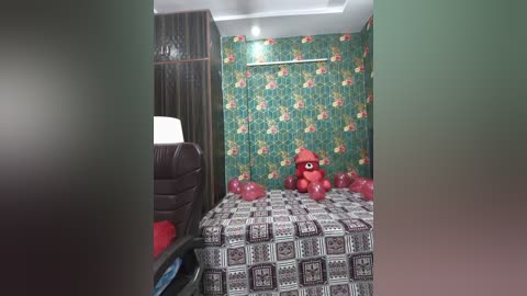Video of a small, cozy bedroom with green floral wallpaper, a bed with red patterned bedding, a plush red teddy bear, and a framed photo on the wall.