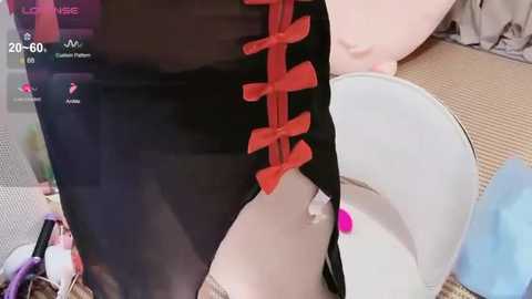Video of a person wearing a black and red Chinese-style qipao dress, with a close-up view of the back, featuring red buttons and a pink hairpin. Background includes a white bucket and a blue object.