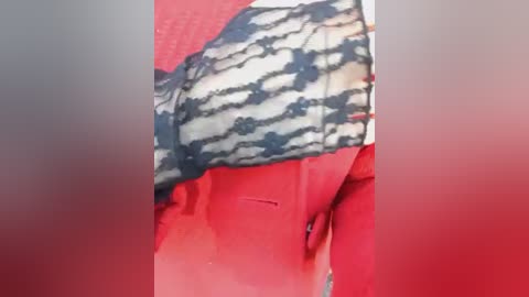 Video of a person wearing a black and white striped shirt with red sleeves, leaning against a red wall. The image has a blurred background, emphasizing the vibrant colors and patterns of the clothing.