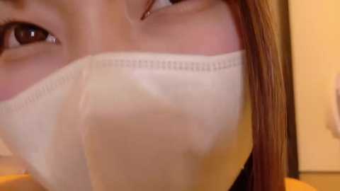 A close-up video of a person's face partially obscured by a white medical mask, highlighting the eyes and nose, with brown hair in the background.