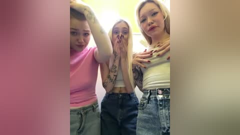 Media: Video of three young women with different hairstyles and attire, standing close together, hands on heads, in a brightly lit room with a yellow wall.