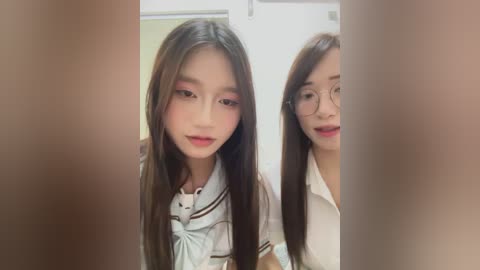 Video of two young Asian women with long black hair, wearing school uniforms. The foreground is blurry, while the background shows a classroom setting.