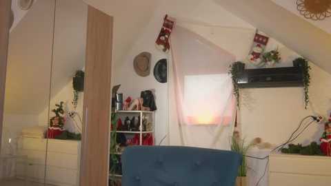 Video of a cozy attic bedroom with a blue upholstered chair, white shelves filled with shoes and decor, Christmas tree, and festive decorations.