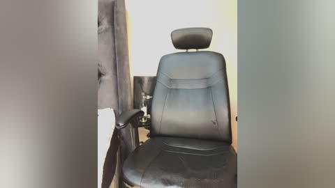 Video of a black leather office chair with a high backrest and headrest, positioned against a frosted glass wall and a white wall, creating a minimalist, modern office setting.