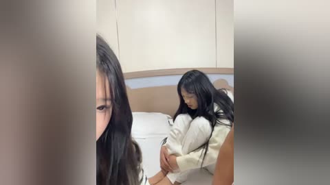 Video of two young Asian women with long black hair, one in a white nightgown, hugging the other, who's partially obscured by a curtain.