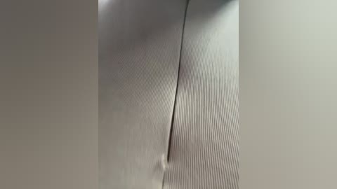 Video of a close-up, textured fabric with vertical stripes, slightly puckered, creating a subtle three-dimensional effect against a neutral background.