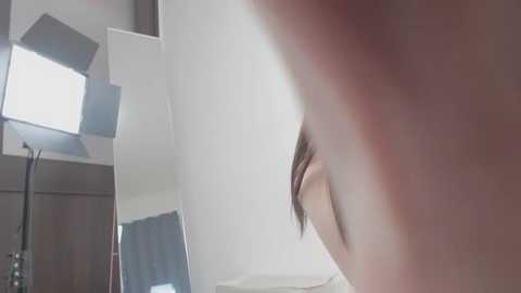 A close-up video of a person's eye with long eyelashes, captured in a modern, minimalist setting with white walls and rectangular light fixtures. The image has a slightly out-of-focus effect, emphasizing the eye's detail.