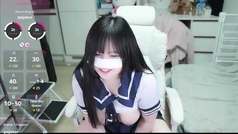 Video of an Asian woman with long black hair and bound breasts in a white office chair, wearing a navy blue schoolgirl uniform.