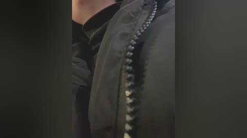 A close-up video of a person's arm in a dark jacket with a metallic zipper, partially obscured by shadows. The texture of the jacket appears smooth and slightly reflective.
