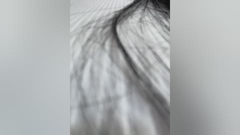 A close-up video of a person's hair, showing a textured, wavy, and slightly unkempt black mane, with a blurred, light-colored background suggesting a neutral, possibly plain backdrop. The image has a soft focus, emphasizing the natural texture of the hair.