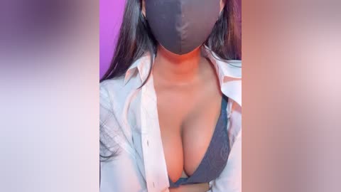 Video of a woman with long dark hair, wearing a black face mask and an unbuttoned white shirt, revealing a grey bra. The background has purple and pink lighting.