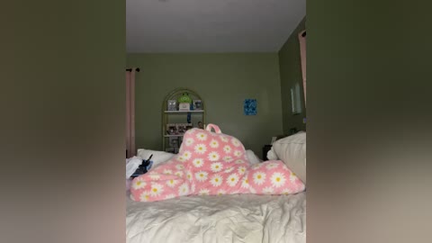 Media: Video of a cozy bedroom with green walls, a white bed, a pink and yellow floral blanket, a bookshelf, and curtains.