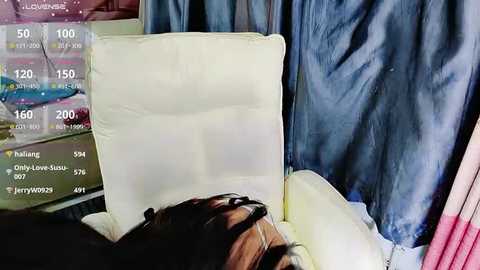 Media: Video of a person lying on a bed, partially covered by a white pillow, with a dark-haired individual in the background, surrounded by blue and pink sheets, with a digital clock displaying 10:00.