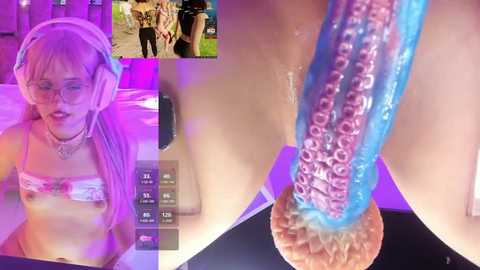A video of a young woman with light skin and long, pink hair, wearing a white headband, pink glasses, and a white lace bra, holding a blue, tentacle-like dildo, with a live-streaming video in the background.