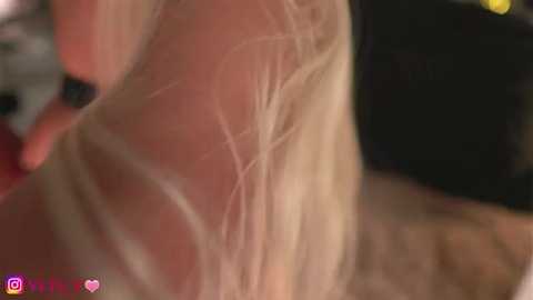 Close-up video of a person with light skin and blonde hair, showing a visible scar across the back of their neck. The background is out of focus, featuring indistinct, blurred objects.