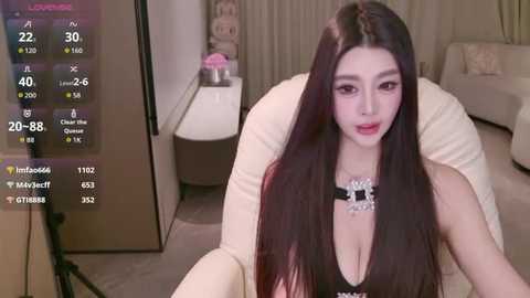 Media: Video of a young Asian woman with long black hair, wearing a black top, sitting on a beige couch in a modern, beige-toned living room.