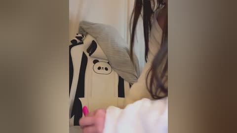 Video of a woman with long brown hair wearing a white sweater, holding a black-and-white panda plush toy.