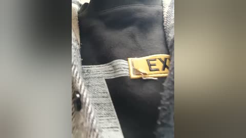Video of a close-up view of a person's hand holding a black jacket with a yellow zipper pull featuring the word \"EX\" in bold letters. The jacket has a textured, woven fabric.
