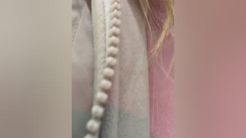 A close-up video of a person's face, focusing on a light beige zipper and a pink sweater, with a blurred background.