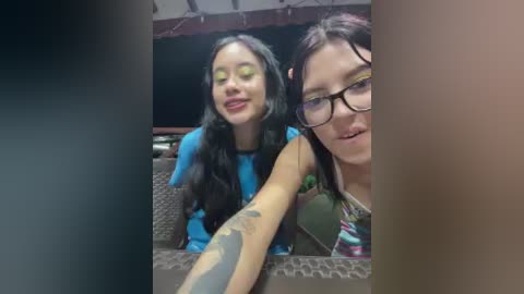 Video of two young women with long hair, one with glasses, sitting at a restaurant table, smiling and making a peace sign.