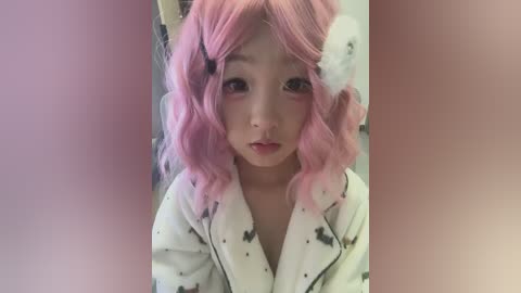 Media: Video of an Asian woman with pink, wavy hair styled with white bunny ears, wearing a white robe with black polka dots, standing indoors with a blurred background.