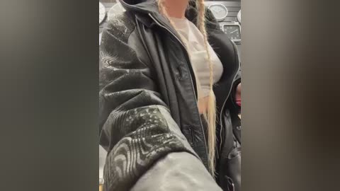Video of a woman wearing a black, puffy jacket with a white shirt underneath, captured in a dimly lit indoor setting with blurred background.