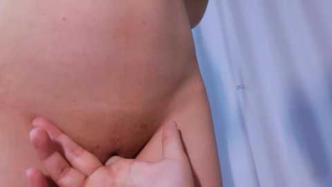 A close-up video of a person's lower abdomen, showing a slight bulge, with a hand gently touching the skin. The background features a light blue curtain.
