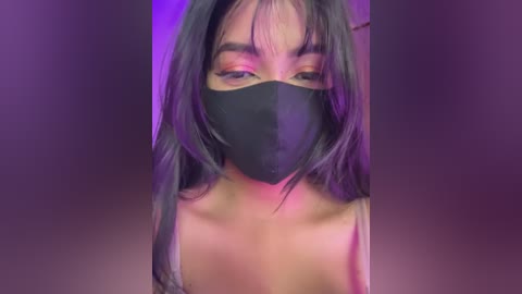 Video of a young Asian woman with long black hair, wearing a black face mask and a tank top, against a purple background.