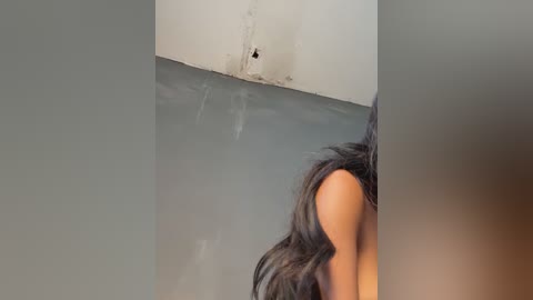 Media: A video captures a woman's back and long, dark hair against a plain, light gray wall with a small, dark hole near the ceiling.