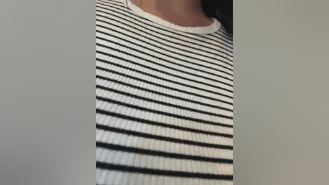 Video of a person's upper torso wearing a white ribbed tank top with black horizontal stripes, against a plain, light gray background.
