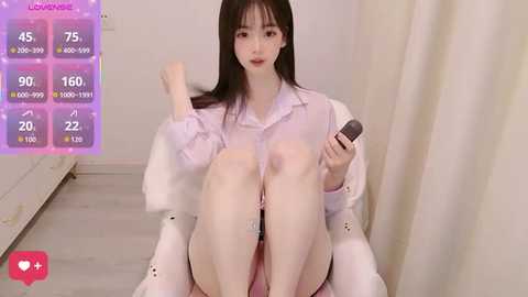 Media: Video of an Asian woman with long black hair, wearing a white shirt, sitting on a chair, holding a microphone, in a white room with a colorful digital panel.