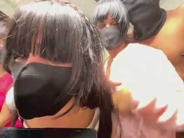 Video of a person with long, straight black hair and a black mask, surrounded by others wearing similar masks, in a crowded, possibly indoor setting.