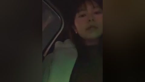 A blurred video of a young Asian woman with long black hair and a neutral expression, captured from an angled, dimly lit perspective.