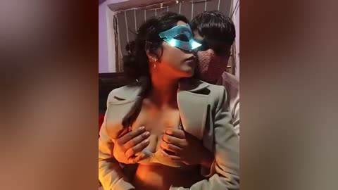 A video of a woman in a blue mask and a gray blazer, holding a man's face, in a dimly lit room with curtains.