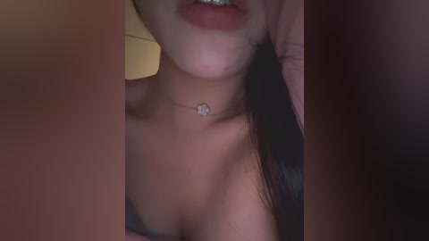 Video of a woman with fair skin, dark hair, and a silver necklace, partially visible, showing her bare shoulders and upper chest.