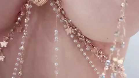Close-up video of a delicate, ornate silver necklace with small, dangling beads and star-shaped charms, adorned with a golden pendant, hanging from a pale-skinned person's neck.