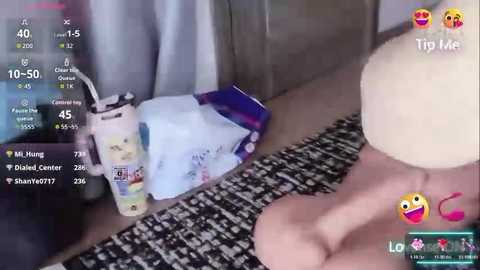 Video of a woman's bare feet on a black-and-white patterned rug, with a plush toy and a water bottle nearby, overlayed with social media text and emojis.